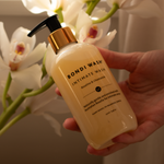 Hand holding a bottle of Bondi Wash intimate wash with flowers in the background