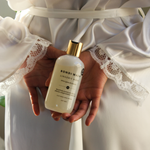 Person holding a bottle of Bondi Wash lingerie wash in a white robe with lace details.